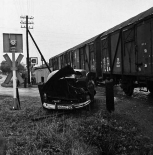 Siebenbäumen (Kreis Herzogtum Lauenburg): Bahnstrecke zwischen Bad Oldesloe und Ratzeburg: Bahnübergang der Landstraße zwischen Bad Oldesloe und Ratzeburg: Filmaufnahmen der Reginald Puhl Filmproduktion aus Hamburg-Wandsbek zum Dokumentarfilm "Todesfallen": nachgestellter Bahnunfall einer Dampflokomotive mit einem Pkw: in der Mitte beschädigter Pkw: dahinter Bahnübergang: rechts Güterwaggons: links Signalanlagen, Wartehäuschen und Strommast: dahinter Straße mit parkenden Pkws, Fußgängern und Bäumen