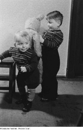 Zwei Kinder, eines spielt mit einem Teddybären