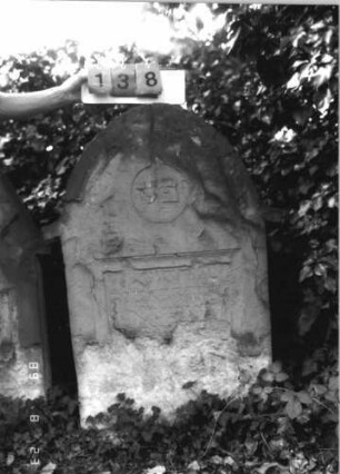 Grabstein 138 (Index: 100110695) Material: ? Zustand: untere Hälfte gänzlich verwittert, Abschieferungen im Giebel, sehr großer Textverlust Maße HxBxT: 122x77x14 cm Beschreibung: Stele, Rundbogenabschluß mit Ohren, Schriftfelder eingetieft Besonderheit: siehe freie Kommentierung: Grabstein 138