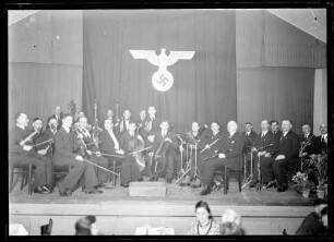 Musikkapelle auf Bühne sitzend, dahinter Reichsadler