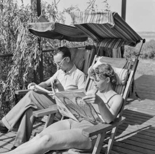 Elisabeth Gremmler und ein Mann lesen in Klappstühlen sitzend die Zeitschrift "Die neue Linie" und ein Buch