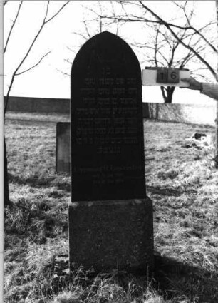 Grabstein 16 (Index: 100116099) Material: Granit, poliert Zustand: gut Maße HxBxT: 177x52x18 cm Beschreibung: aufgesockelte Stele mit Spitzbogenabschluß Symbolik: Levitenkanne, Schofar Besonderheit: kulturhistorisch wertvoll / hist.-wiss. Gründe (Gemeindestellung): Grabstein 16