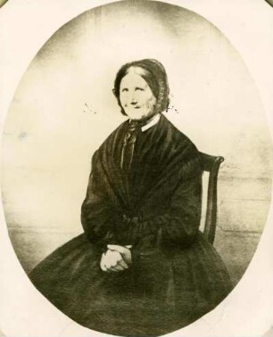 klassisches Portrait einer alten Dame im Sonntagskleid, sitzend auf Stuhl. Oval berahmt