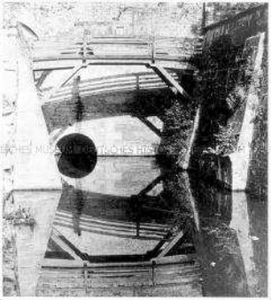 Holzbrücke über einem Kanal und ihre Spiegelung im Wasser