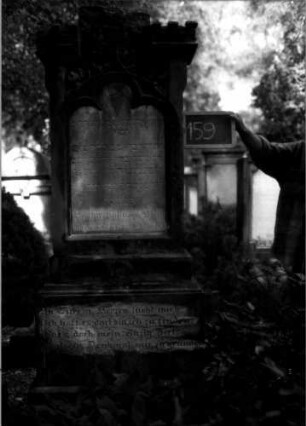 Grabstein 159 (Index: 100109749) Material: Sandstein, Marmorplatte Zustand: verwittert Maße HxBxT: 200x70x33 cm Beschreibung: Stele, getreppter Sockel, getreppter Abschluß, Schriftplatte mit Kleeblattbogenabschluß Symbolik: Maßwerk mit Blättern, Zinnen auf den Abschlußeinzügen: Grabstein 159