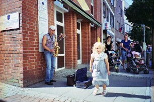 Hindenburgstraße: links Saxophonspielerin, rechts Fußgänger mit Kindern