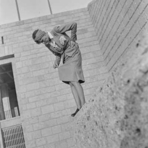 Frau im Kostüm sitzt auf einer Mauer
