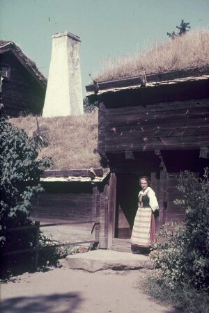 Reisefotos Skandinavien. Junge Frau in Tracht vor einem Holzhaus (vielleicht einer Räucherei)