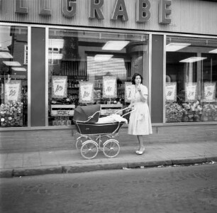 Frau mit Kinderwagen auf einem Gehweg vor einem Laden