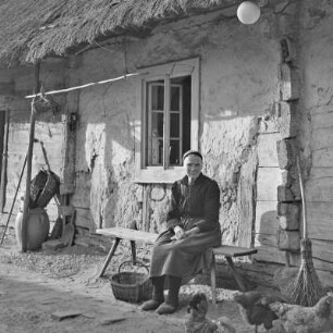 Strohgedecktes Blockhaus in Burg-Kauper. Frau Nowick in Spreewälder Alltagstracht vor ihrem Gehöft. : Ze słomu skryte kładźity twar statoka w Kupaŕskich Bórkowach. Knjeni Nowickowa we wšědnej Błótowskej drasće před swojim statokom.