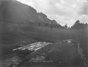 Landschaftsblick : Ein Bach, der von einer Brücke überspannt wird, vor Berghängen mit einzelnem Baumbestand
