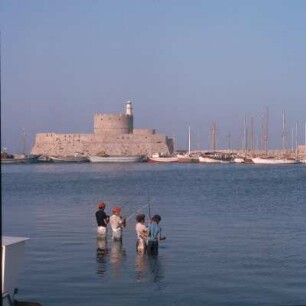 Rhodos (Stadt). Fort Agios Nikolaos, Mandraki-Hafen. Einheimische Hobby-Angler. Drüben Fort Agios Nikolaos von 1464 und 1480