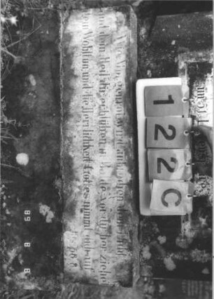 Grabstein 122 (Index: 99800074) Material: Sandstein, Schriftplatten Marmor Zustand: verwittert, Schriftplatte gesprungen Maße HxBxT: 162x56x24 cm Beschreibung: Stele, Mittelerhöhung, Zinnenaufsatz, eingelassene Schriftplatte mit Kleeblattbogenabschluß, getreppter Sockel, im oberen Teil weitere Schriftplatte eingelassen: Grabstein 122C