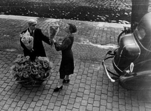 Amsterdam 1936. Eine Frau kauft auf einer Straße von einem Blumenverkäufer ein Strauß. Hier sind es aber nicht typisch holländischen Tulpen