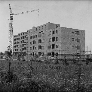 Fuchsberg / Im Hölk: Wohnblocks der Gemeinnützigen Wohnstätten Genossenschaft Bad Oldesloe: im Bau mit Gerüst: davor Baumaterial: hinten links Baukran: vorn verkrautete Wiese