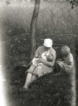 Bäuerin beim Stillen und daneben sitzendes Mädchen am Feldrand