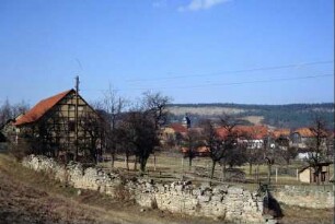 Ortsrand mit Natursteinmauern aus Kalkstein, Obstwiese, Scheune; hinten Kirche