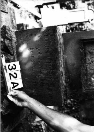 Grabstein 32 (Index: 99801980) Material: Sandstein Zustand: hebräische Schrifttafel fehlt Maße HxBxT: 134x50x25 cm Beschreibung: Stele, getreppter Sockel, eingezogener Rundbogenabschluß mit Verdachung, eingetieft. Schriftfeld mit Rundbogen Symbolik: achtzackiger Stern, Blätter: Grabstein 32A