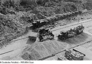 Dresden. Blick auf eine Baustelle zwischen Trümmern, Kipplorenzug der Trümmerbahn wird beladen - Lastkraftwagen mit Baustoffen werden entladen