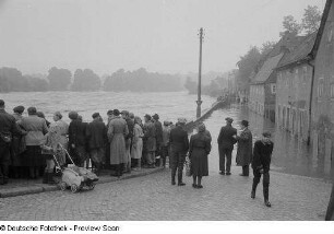 Menschen an einer Mauer, auf das Hochwasser schauend