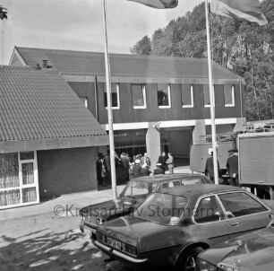 Bünningstedt: Freiwillige Feuerwehr Bünningstedt: Dorfstraße: Einweihung des neuen Feuerwehrgerätehauses: vorn parkende Pkws und Fahnenmasten: links Löschfahrzeug mit Feuerwehrmännern: hinten Mitte vor Gerätehaus Gäste