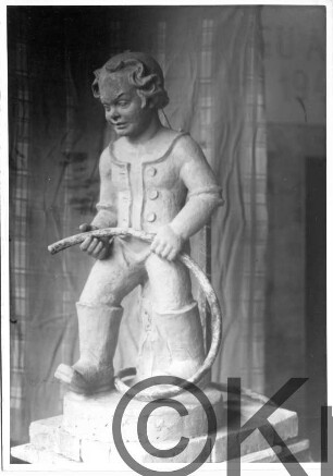 Knabe in Stiefeln mit Wasserschlauch: Tonmodell auf Sockel: in Atelier, hinten Vorhang;
