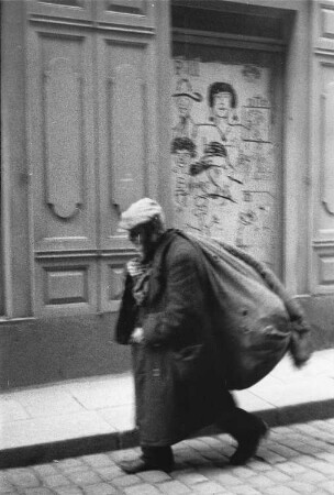 Mann mit Jutesack auf dem Rücken, an der Hauswand Kohlezeichnungen, vermutlich in Dresden