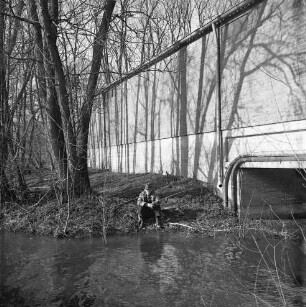 Trave: vorn Mitte Angler am Ufer: dahinter Johannes Ströh Mühlenwerke (Weizenmühle) mit Wasserdurchlass: links Bäume