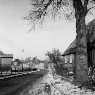 Hauptstraße: vorn rechts Baum: dahinter Jägerzaun, Vorgarten und Haus: hinten links Strommasten, Bauernhäuser und Bäume: Winter