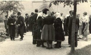 Frauen zum Teil in Kirchgangstracht und Männer in Schleife vor der Kirche : Žony zdźěla w Slepjanskej drasće a mužojo před Slepjanskej cyrkwju