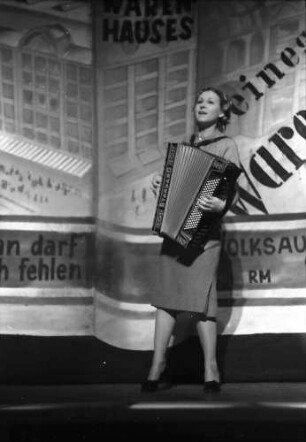 Berlin: Kabarett der Komiker; Ruth Tuxedo spielt Schifferklavier vor Warenhausprospekt