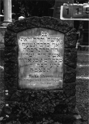 Grabstein 115 (Index: 100101632) Material: Granit, weiße Marmorplatte Zustand: Platte quer gesprungen, verwittert Maße HxBxT: 103x62x19 cm Beschreibung: Stele, rustica, Sockel, Segmentbogenabschluß, Schriftplatte: Grabstein 115