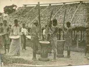 In Ketten gelegte afrikanische Gefangene mahlen Getreide vor einem Haus