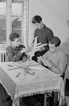 Jungen beim gemeinsamen Bau von Segelflugzeugmodellen, vermutlich in einem Wohnheimzimmer