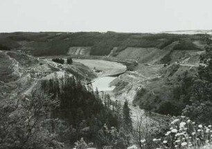 Bau der Bleilochtalsperre : Bau der Bleilochtalsperre bei Saalburg. Baustelleneinrichtung mit Gerüstbecken der Feldbahn, Baugrube der Staumauer, Fangedamm und teilweise abgeholzten Südwesthängen des künftigen Stauraumes. Blick von den Bleibergen nach Südwesten