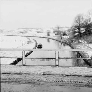Trave mit Kahn: vorn Brückengeländer: hinten rechts an Böschung Bäume: Blick von der Brücke ins Travetal: Winter