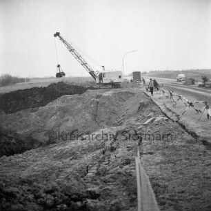 Industriestraße: Absackung eines Teilstücks: vorn Abbruchkante mit Grube: rechts Absperrung: dahinter Bagger, Arbeiter, Baubude, Baumaschinen und Pkw