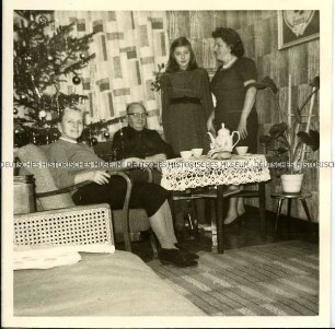 Familienmitglieder am Kaffeetisch vor dem Weihnachtsbaum