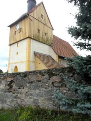Ansicht von Nordosten mit Kirche (Kirchturm romanischer Chorturm) über Kirchhofmauer (Wehrgang mit Schießscharten abgetragen) mit Werksteinen im Mauersteinverband