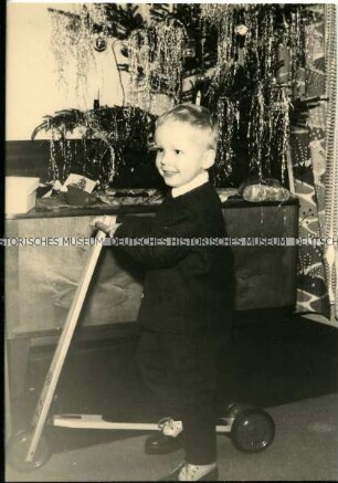 Kleiner Junge mit Tretroller unter dem Weihnachtsbaum