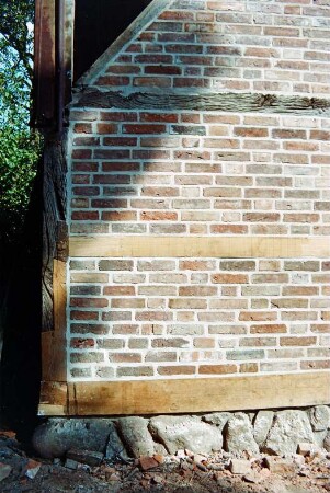 Dorfplatz (2): Fachwerkscheune: Sanierung: Giebelseite, Detailaufnahme: Gebäudeecke, erneuerter Schwellbalken auf Feldsteinfundament, Pfosten und Riegel teilweise nach Erneuerung, Gefache mit neuer Ausmauerung: 8. August 1994