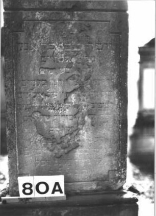 Grabstein 80 (Index: 99898841) Material: Sandstein Zustand: stark verwittert Maße HxBxT: 169x54x26 cm Beschreibung: aufgesockelte Stele, Giebelaufsatz mit Eckakroterien, unterer Sockel felsartig gearbeitet: Grabstein 80A