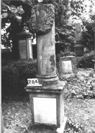 Grabstein 284 (Index: 100082297) Material: Sandstein, weiße Marmorplatte Zustand: leicht verwittert Maße HxBxT: 212x63x57 cm Beschreibung: postamentierte abgebrochene Säule, rechteckige Schriftplatte Symbolik: Kranz um Säule: Grabstein 284