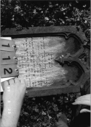 Grabstein 112 (Index: 99792204) Material: Sandstein Zustand: verwittert mit Textverlust Maße HxBxT: 86x48x11 cm Beschreibung: Stele, eingezogener Spitzbogenabschluß, Schriftfeld eingetieft Symbolik: Maßwerk: Grabstein 112 (Detailaufnahme)