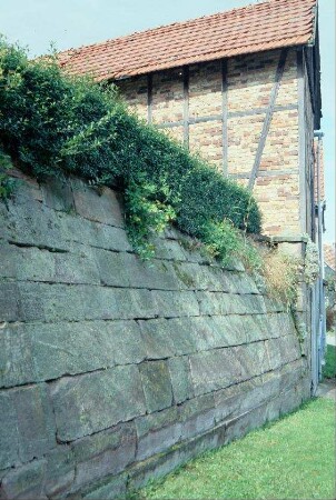 geneigte Bruchsteinmauer und Wirtschaftsgebäude