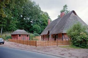 Nütschau: Schloßstraße 42a-c: traufständige Mehrfamilienkate aus Fachwerk mit Reetdach: Straßenfront mit Eingangstüren, Sprossenfenster, Heuluke: Giebelseite, oben Eulenloch: links Nebengebäude: Lattenzaun, hinten Wald
