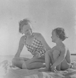 Frau in Bademode und nacktes Kind sitzen am Strand