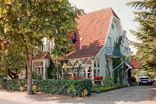 Lindenstraße 14: Stadtvilla: Straßenfront, links Quergiebel, daran Auslucht, daneben Veranda: Giebelseite mit Eingangstür, Balkon: davor Jägerzaun, Hecke, rechts Einfahrt