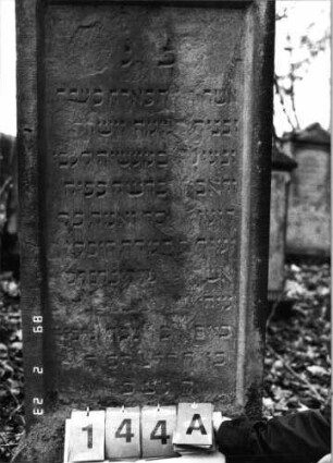 Grabstein 144 (Index: 99751960) Material: Sandstein Zustand: abgeblättert mit Textverlust Maße HxBxT: 160x55x15 cm Beschreibung: Stele, SOckel, Giebel, rechteckiges Schriftfeld eingetieft: Grabstein 144A