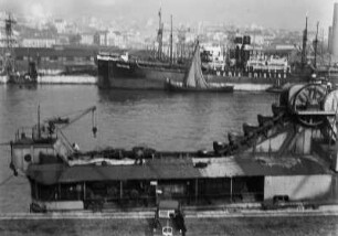 Hafenszene : Schiffe in einem Hafen. Im Hintergrund die Häuser einer Stadt.
